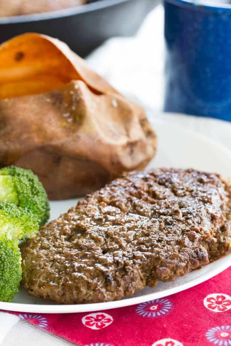 cooked cube steak on a white plate with broccoli and a whole roasted sweet potato.