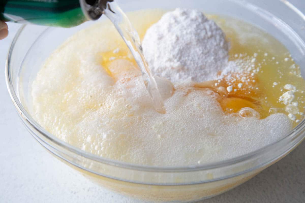 7up soda being poured into a glass bowl filled with cake mix and eggs.