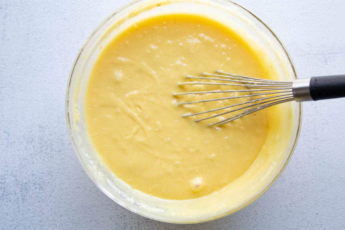 yellow cake batter in a glass bowl with a whisk. 