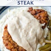 chicken fried steak topped with white gravy on a plate with mashed potatoes and green beans.