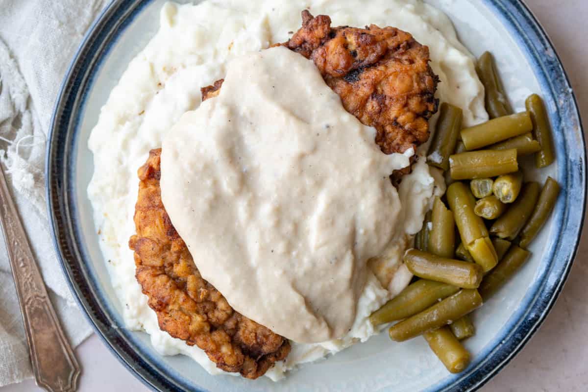 chicken fried steak topped with white gravy, next to mashed potatoes and green beans.
