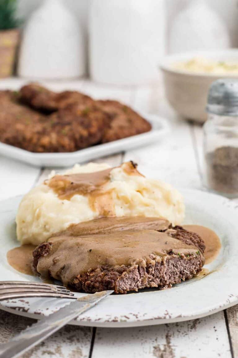 piece of country fried steak and mashed potatoes topped with brown gravy on a white dinner plate.