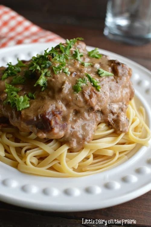 cube steak with brown sauce on a bed of linguine on a white decorative plate.