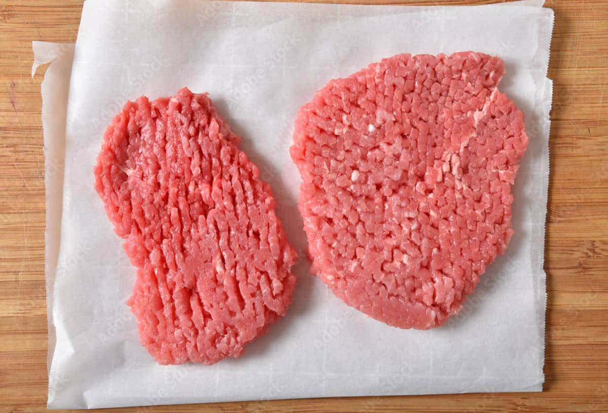 two pieces of raw cube steak on white parchment paper.