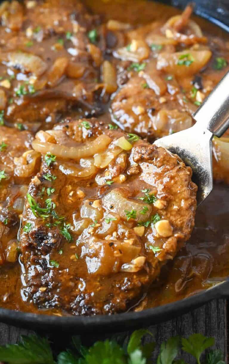 cube steaks in a skillet with a brown onion sauce, topped with chopped parsley.