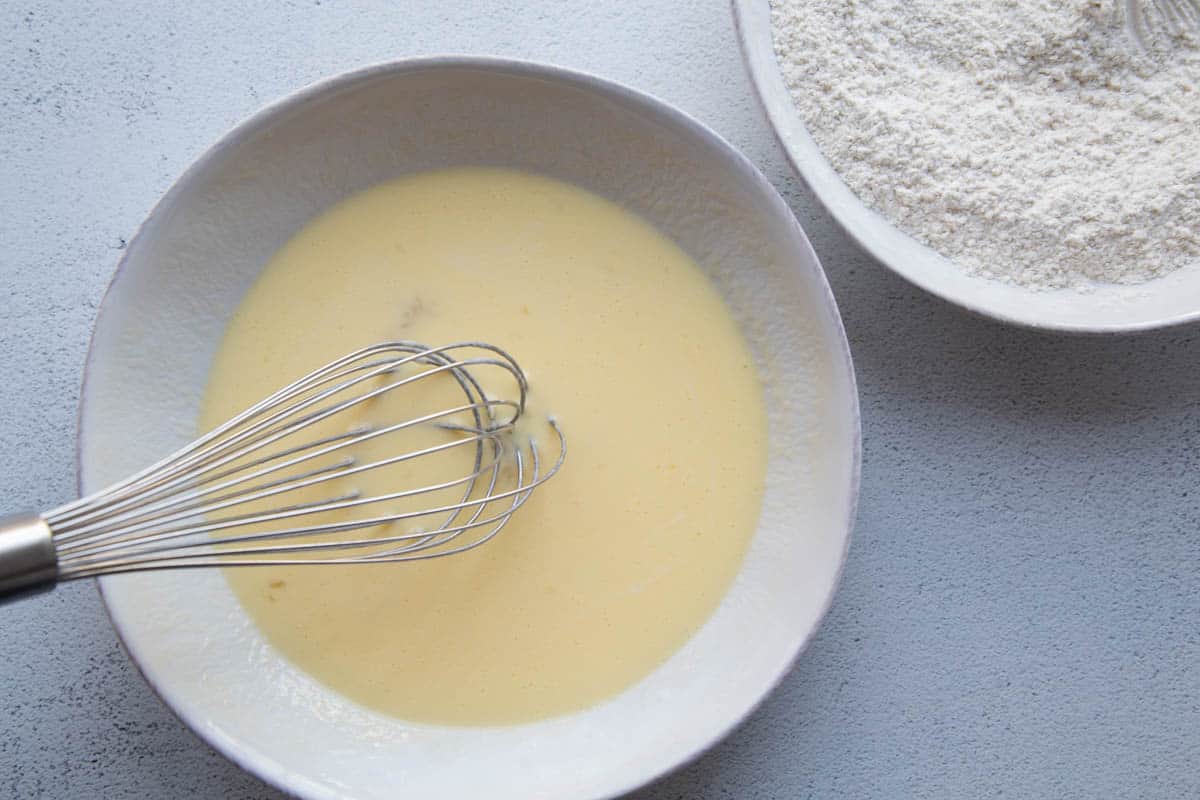 eggs and buttermilk in a shallow white dish with a whisk.