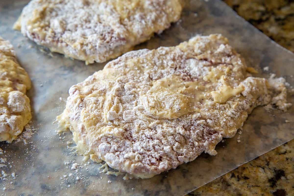 battered uncooked cube steaks sitting on wax paper.