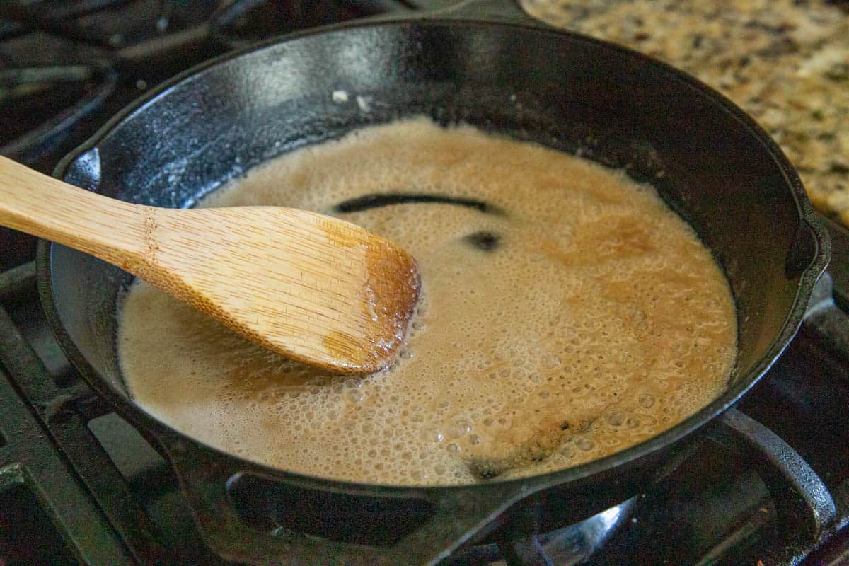 wooden spoon stirring a roux in a cast iron skillet.