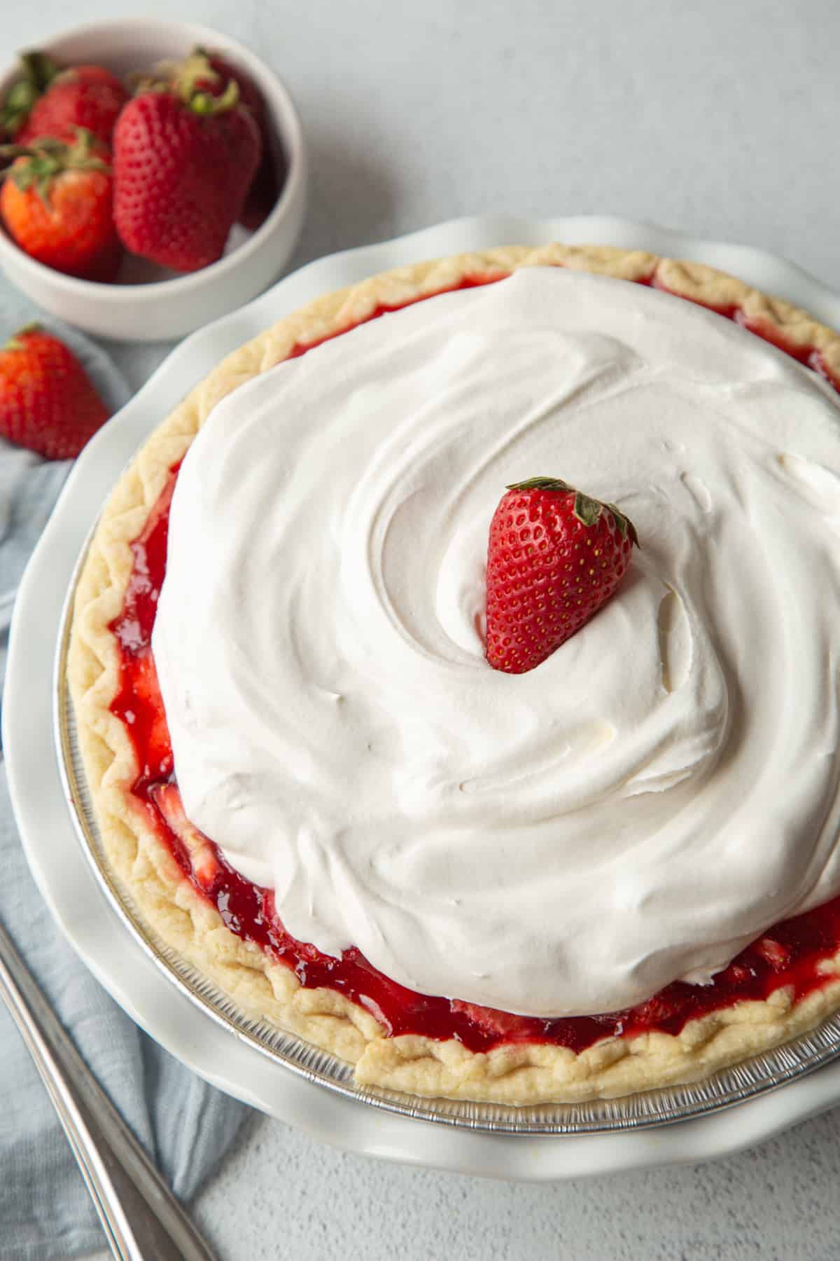 whole strawberry pie topped with whipped cream and a fresh strawberry.