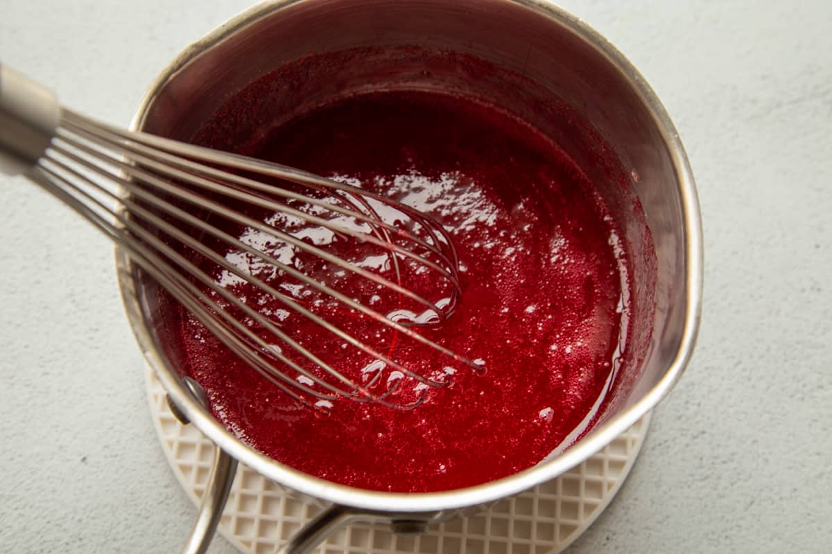 red gelatin mixture in a saucepan with a whisk.