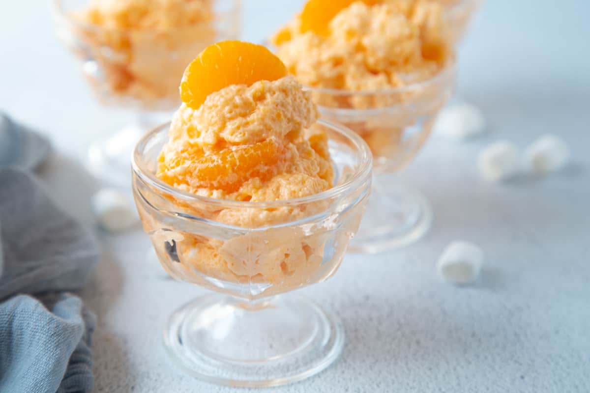 glass parfait dishes filled with orange dreamsicle salad and surrounded by mini marshmallows.