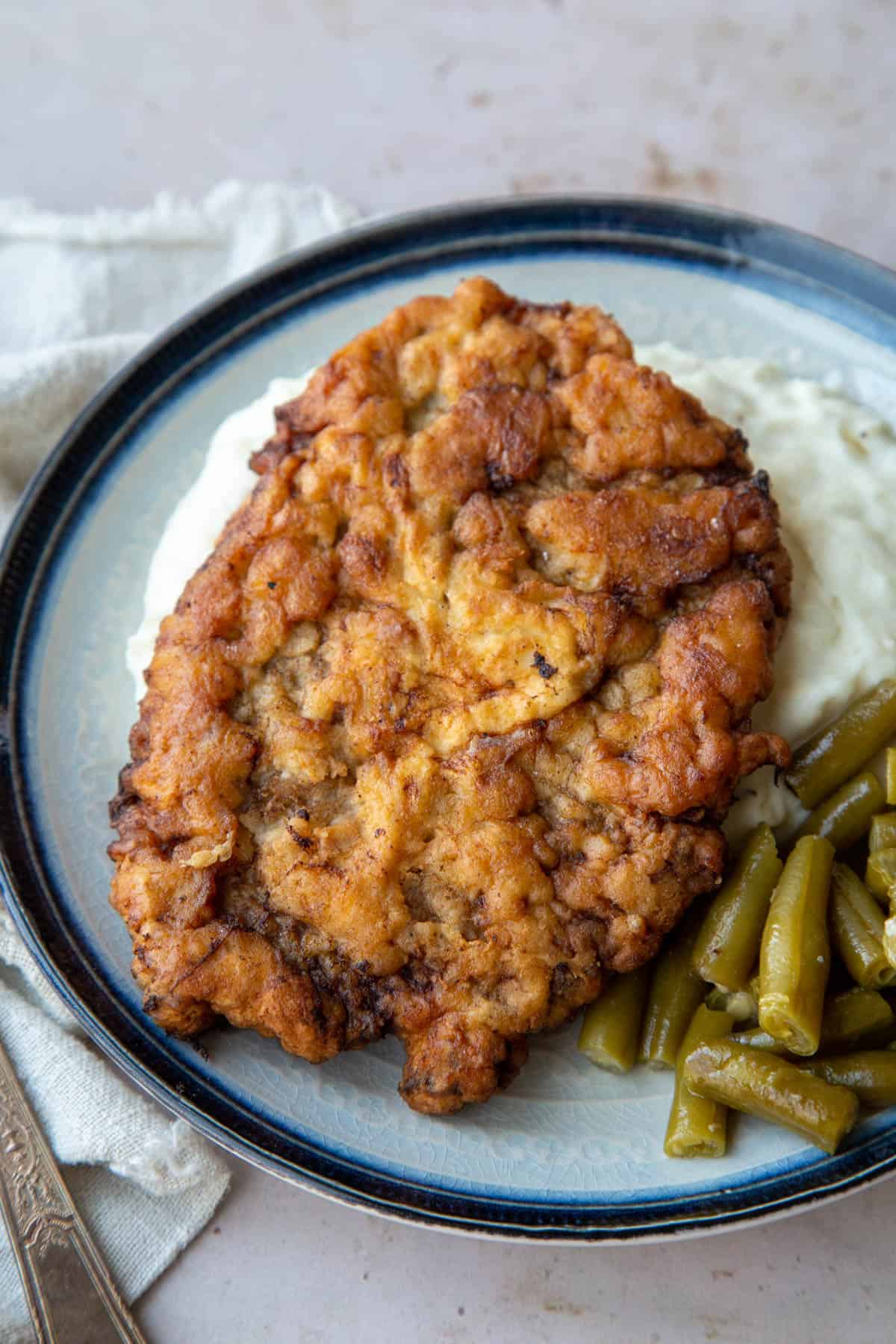 old fashioned chicken fried steak on a plate with mashed potatoes and green beans.