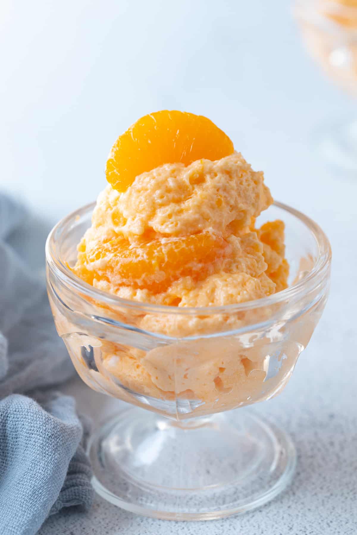 fluffy orange dreamsicle salad in a glass parfait dish, topped with a mandarin orange.