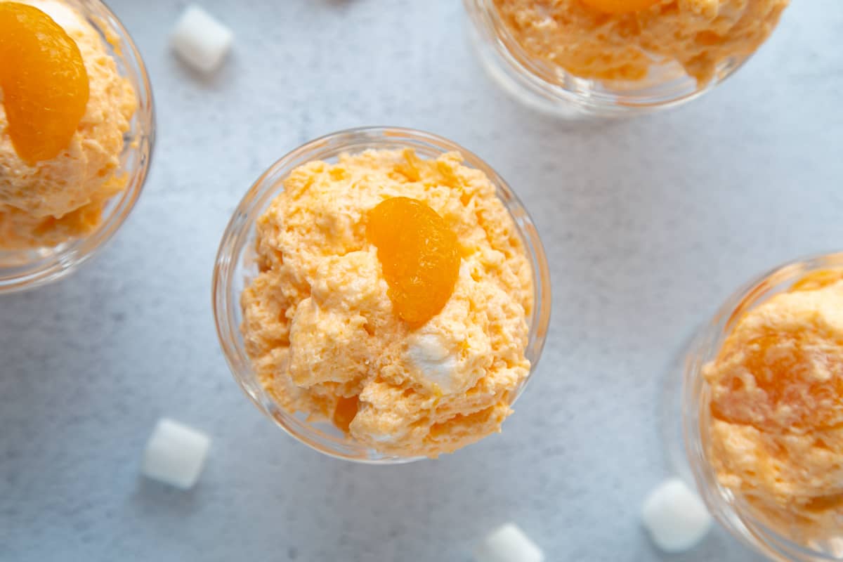 orange dreamsicle salad piled into glass parfait dishes, topped with mandarin oranges and surrounded by mini marshmallows.