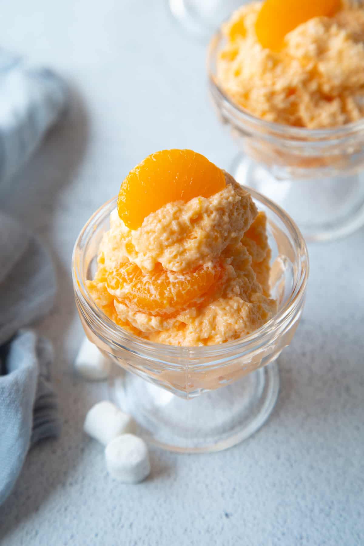 glass parfait dish with fluffy orange jello salad in it, with mandarin oranges on top.