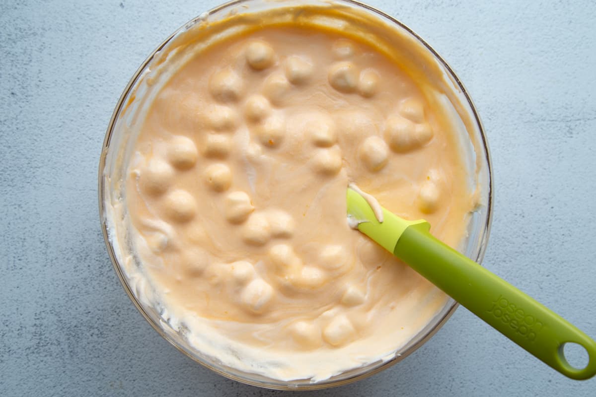 spatula stirring a glass bowl full of a creamy orange mixture with mini marshmallows.