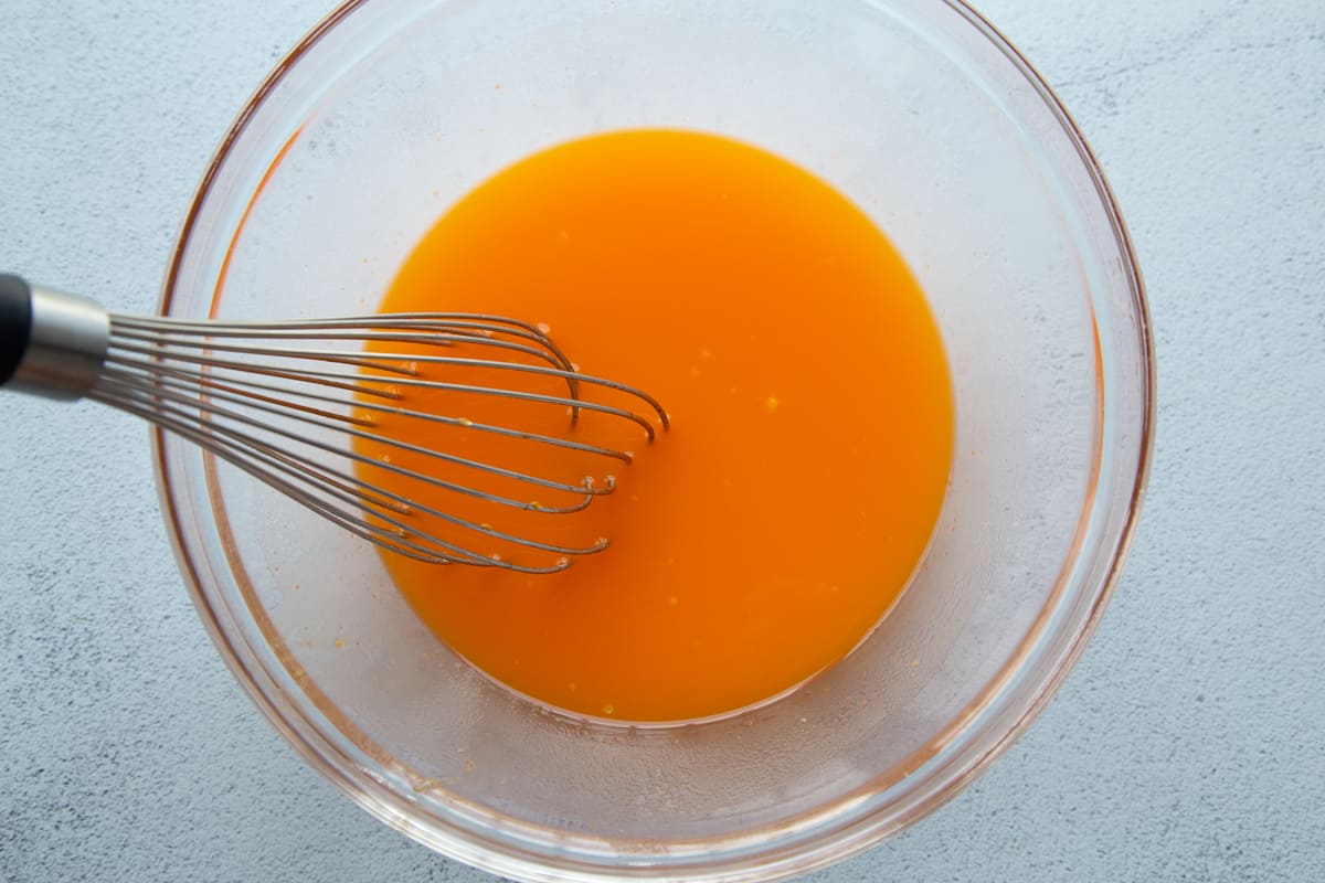 orange gelatin dissolved in water in a glass bowl with a whisk.