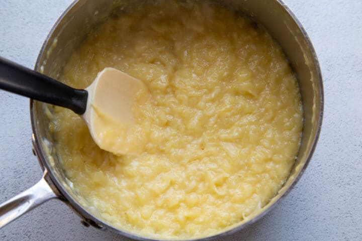 yellow frosting with pineapple and coconut in a large saucepan with a spatula.