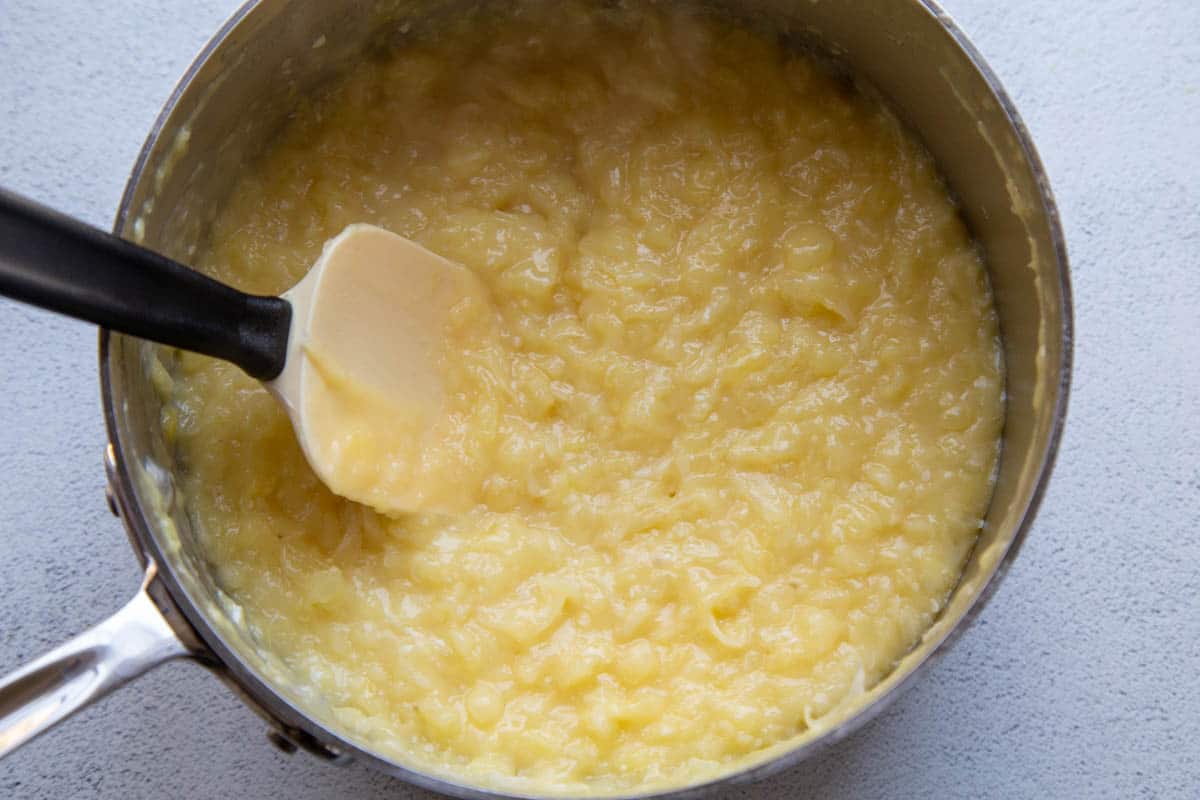 yellow frosting with pineapple and coconut in a large saucepan with a spatula. 