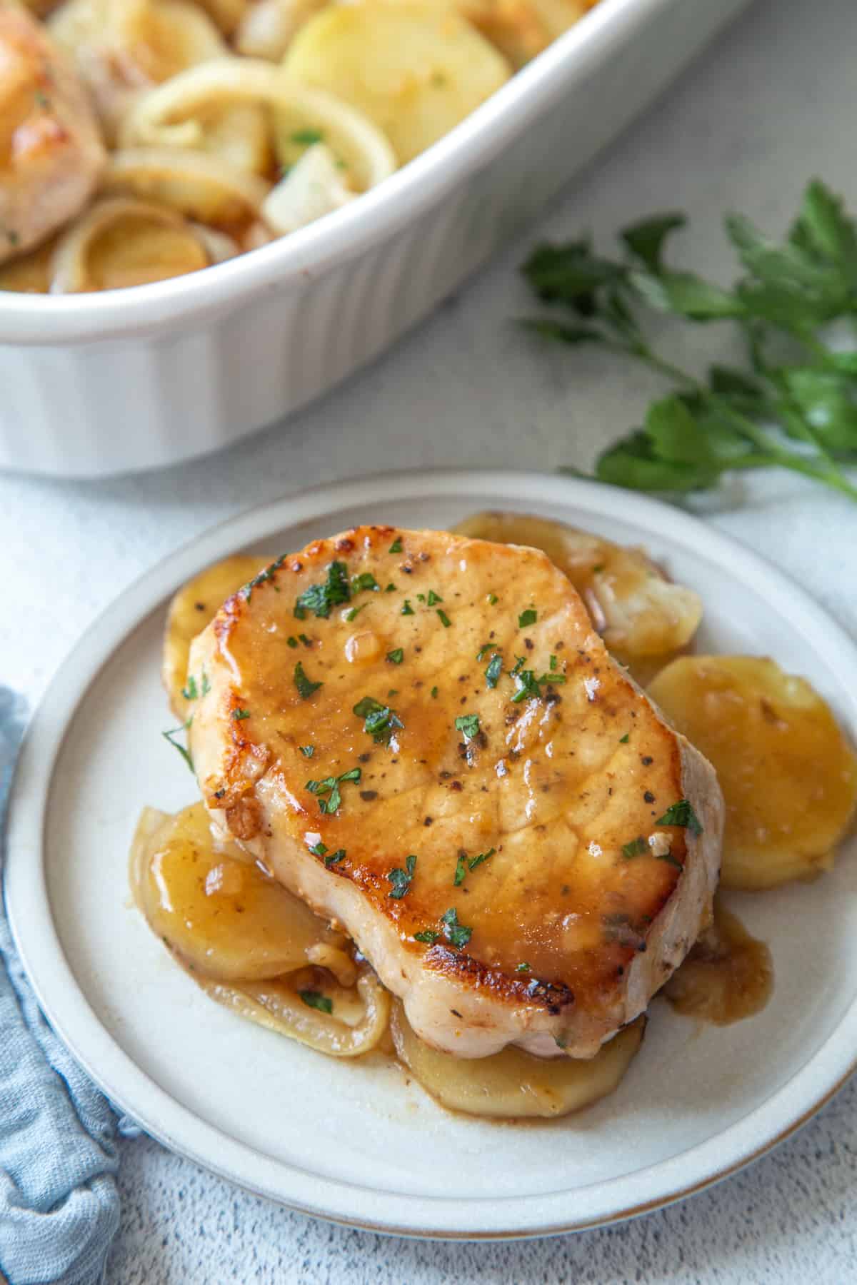 pork chop and potatoes in a brown gravy on a white plate, next to a casserole dish filled with pork chop casserole.