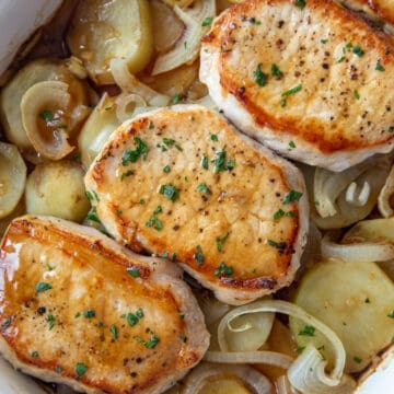 three pork chops on top of sliced potatoes and onions in a casserole dish.