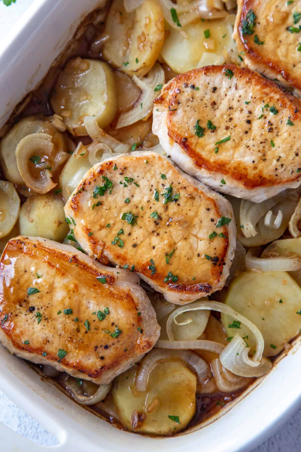 seared pork chops on top of potatoes and onions in a white casserole dish.
