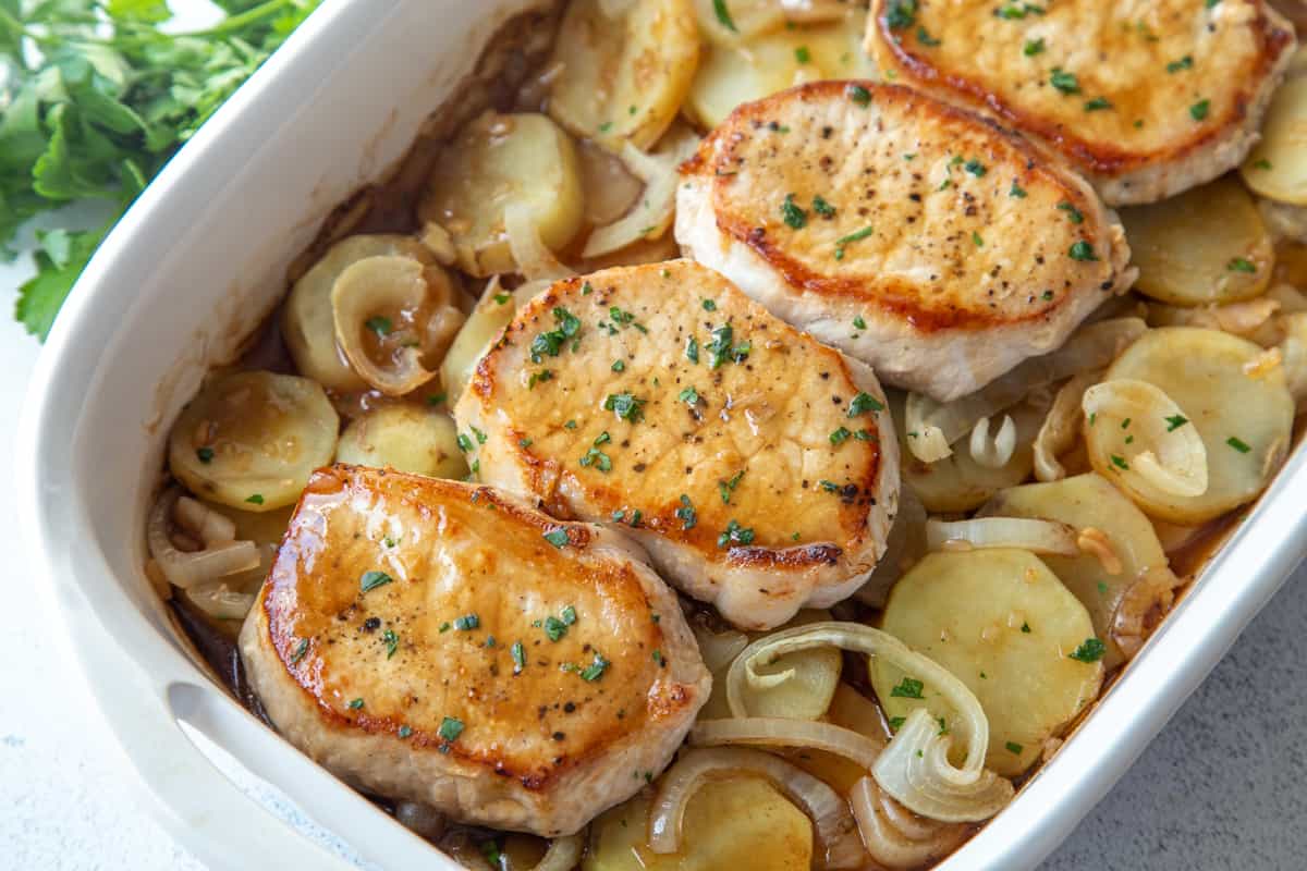 pork chop casserole with onions and potatoes in a white casserole dish.