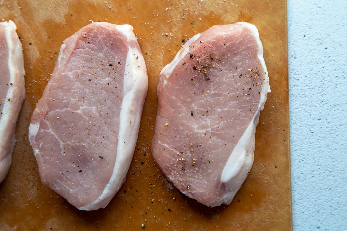 boneless pork chops with salt and pepper on a cutting board.