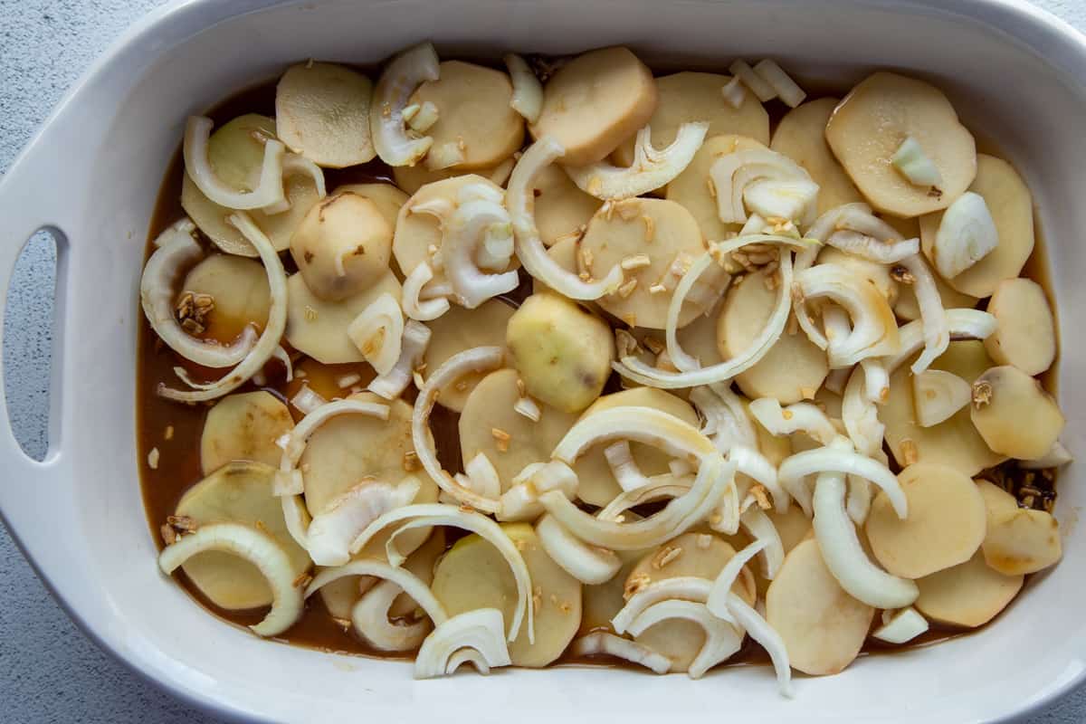 sliced potatoes and onions in a brown gravy in a white casserole dish.