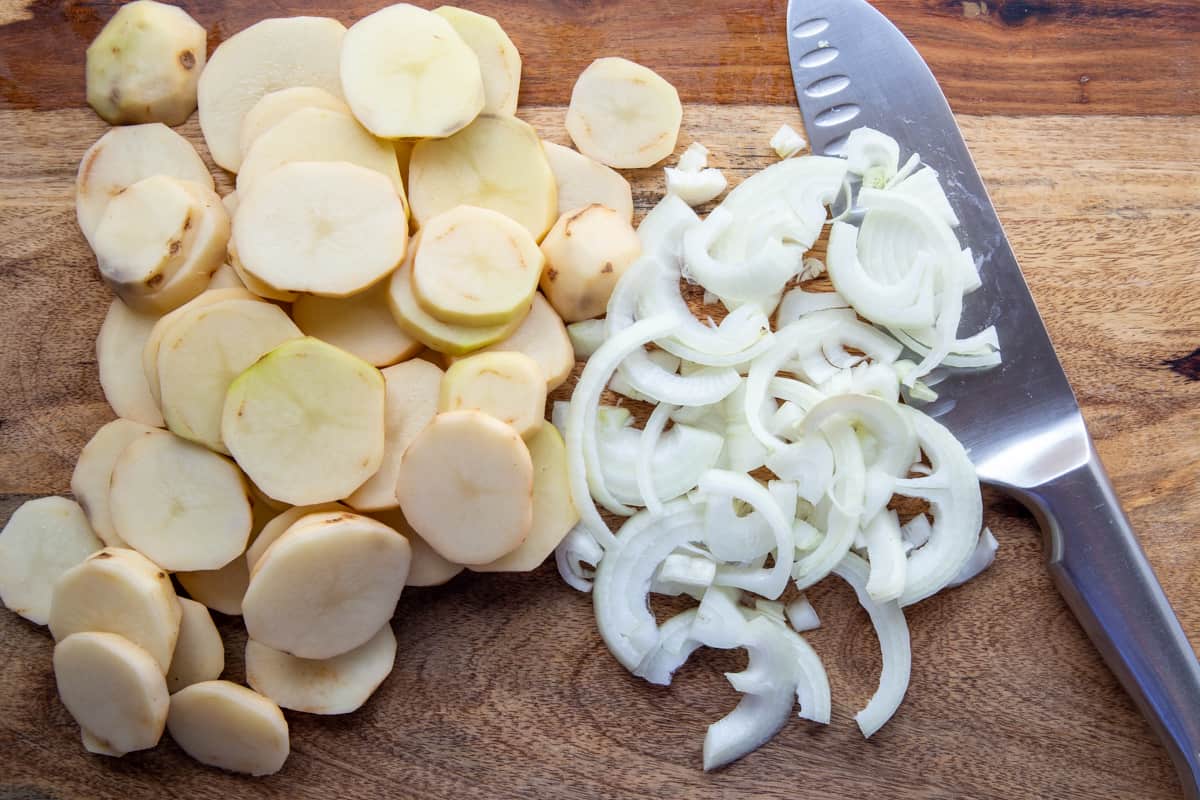 sliced potatoes and sliced onions on a wooden cutting board.