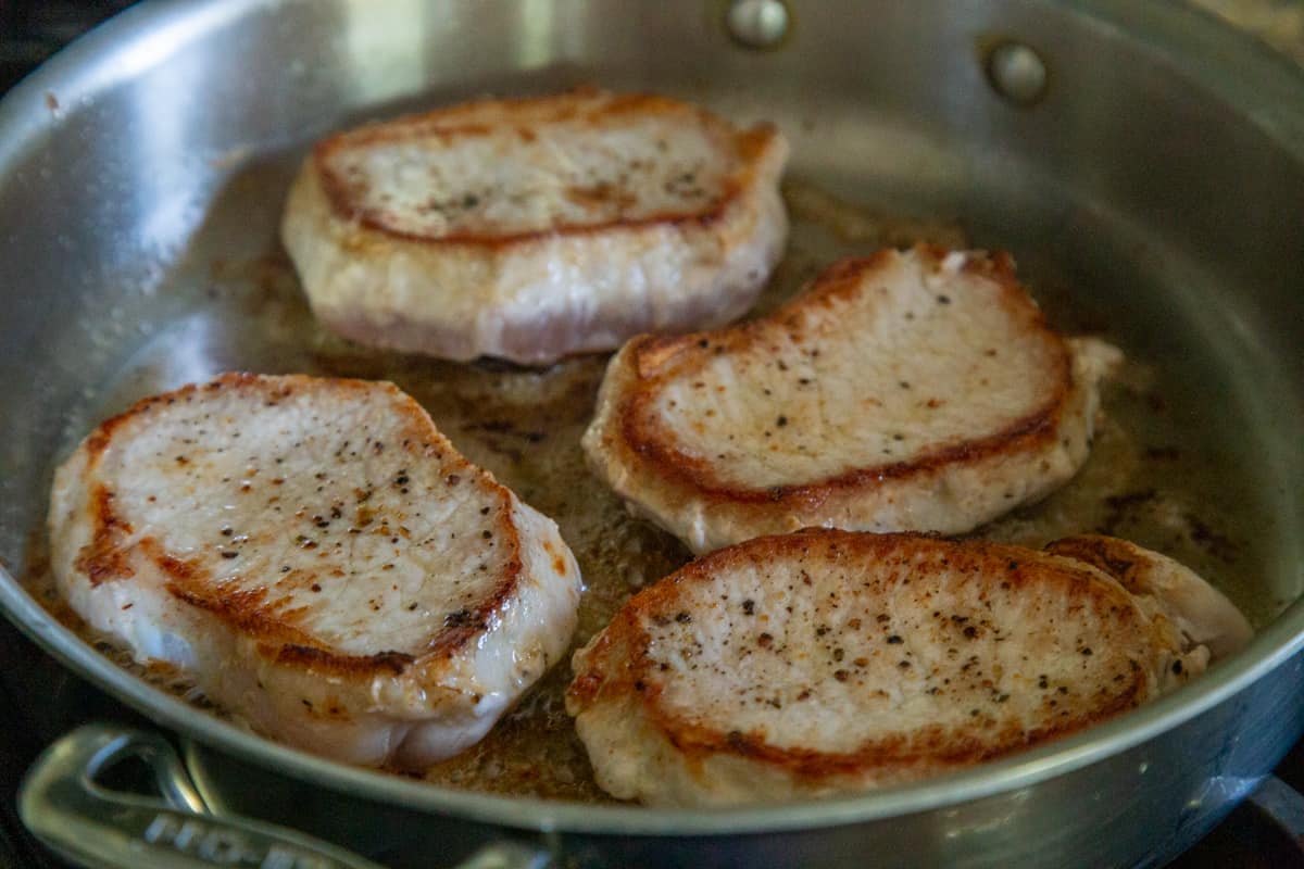 seared pork chops cooking in a metal skillet.