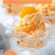 parfait glass filled with an orange gelatin salad topped with a mandarin orange.