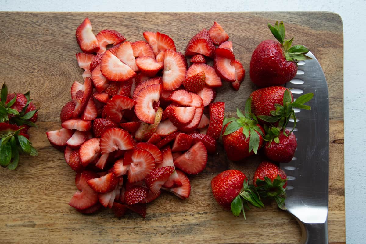 sliced strawberries and a knife on a wooden cutting board.