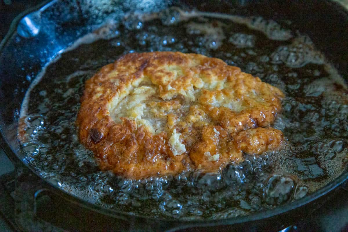 chicken fried steak cooking in oil in a cast iron skillet.