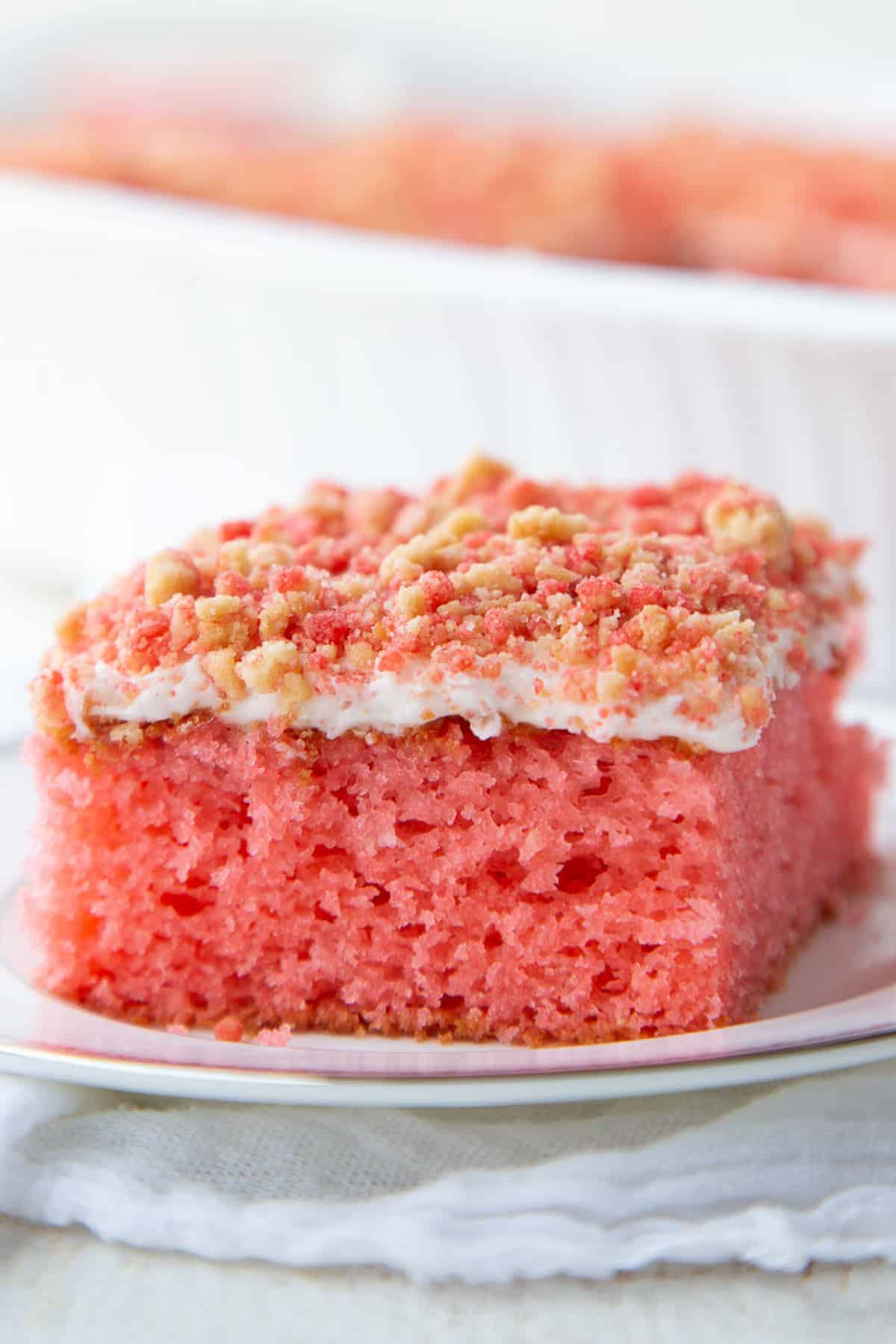 slice of strawberry crunch cake with cream cheese frosting and a crunchy strawberry crumble on top.