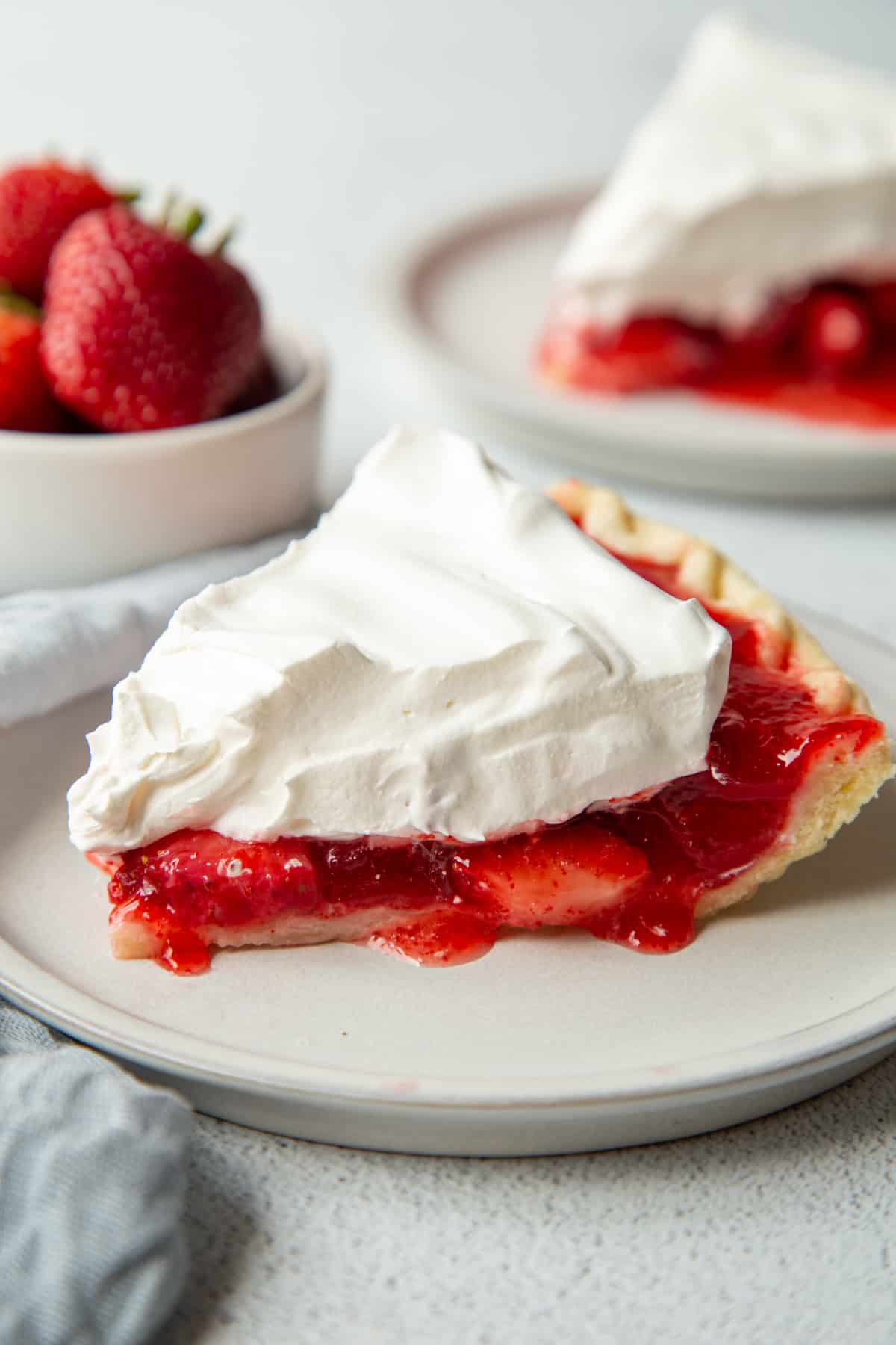 slices of strawberry pie topped with whipped topping on white plates, next to a small dish of fresh strawberries.