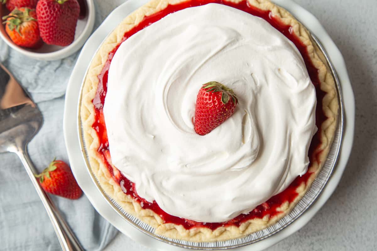 fresh strawberry pie topped with whipped cream and a single strawberry.