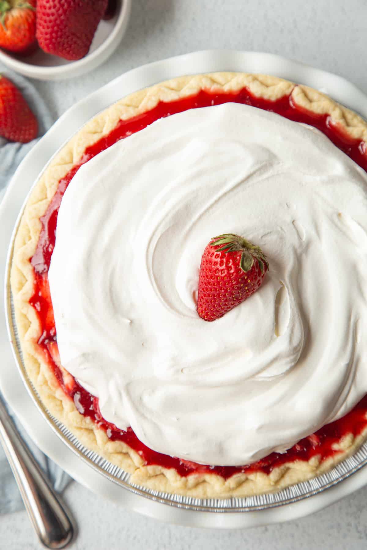 fresh strawberry pie topped with whipped cream and a single strawberry in a white pie dish.