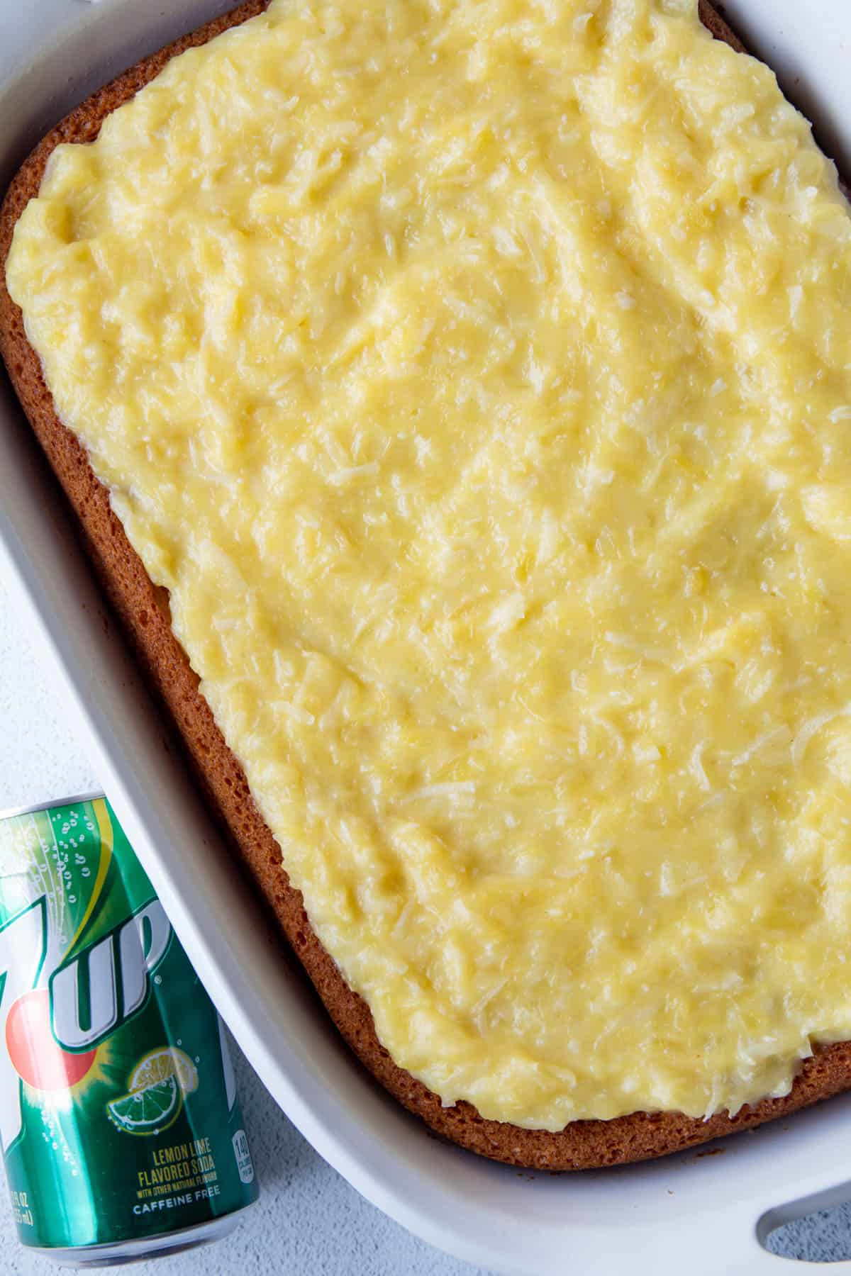 whole 7up cake topped with yellow coconut frosting in a white baking dish next to a can of 7up.