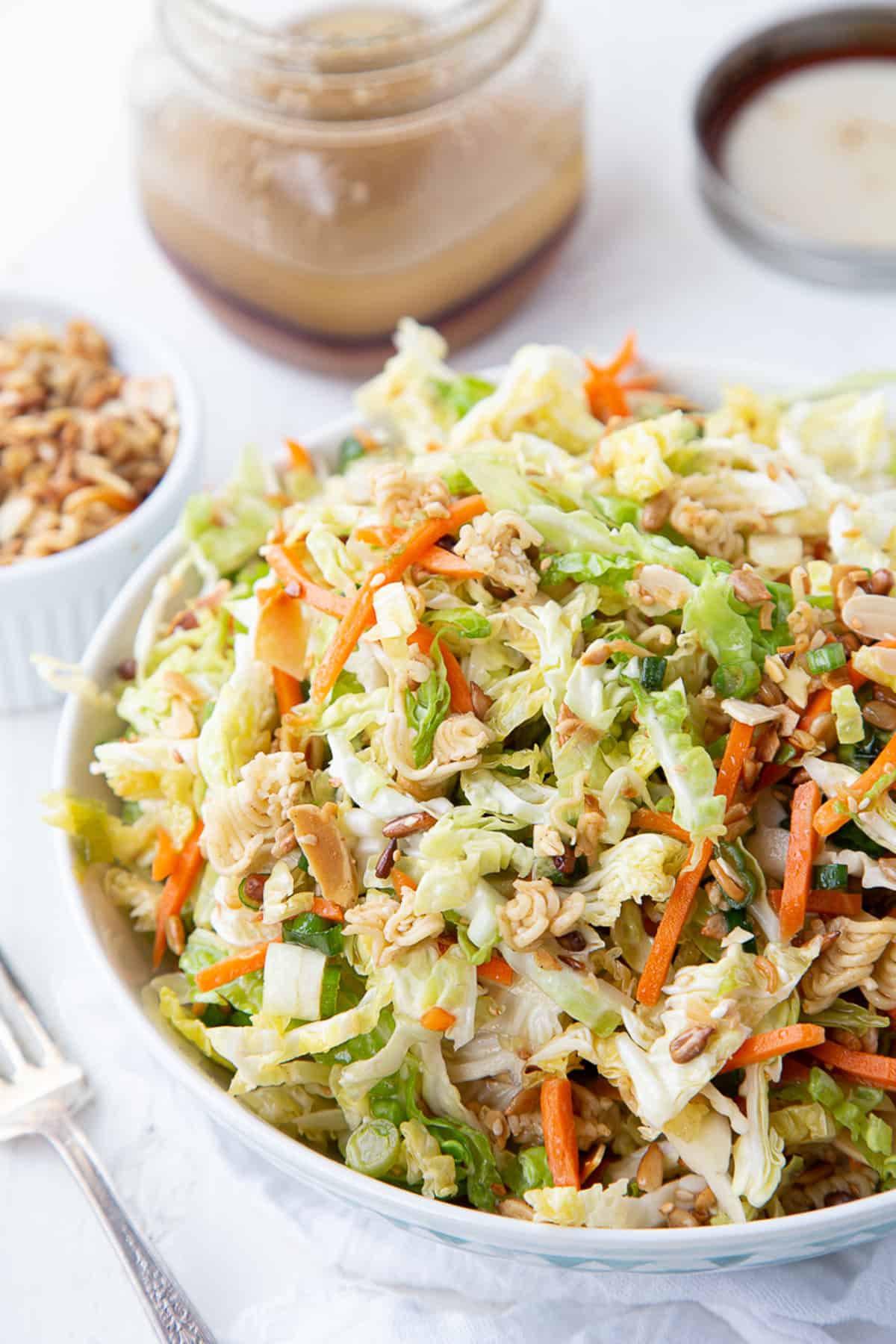 asian cabbage salad with ramen and shredded carrots in a decorative bowl next to a mason jar of asian dressing.