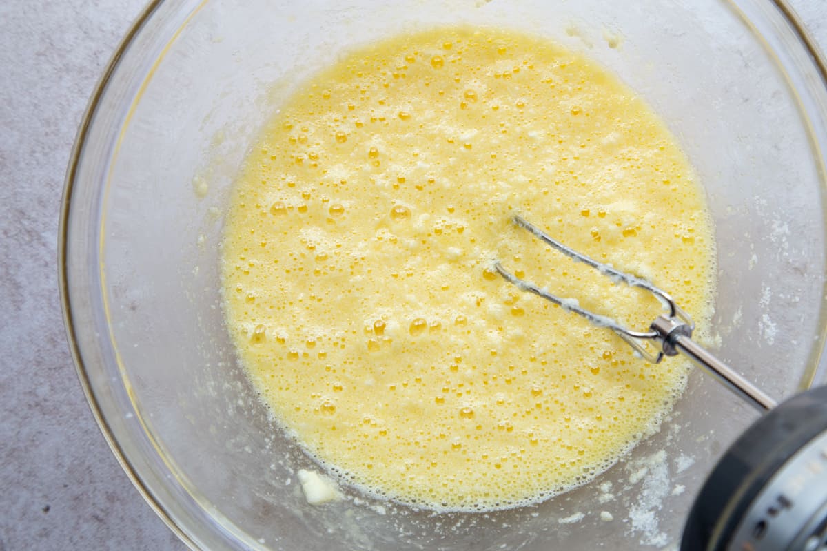 egg, butter, and sugar mixture in a glass bowl with a hand mixer.