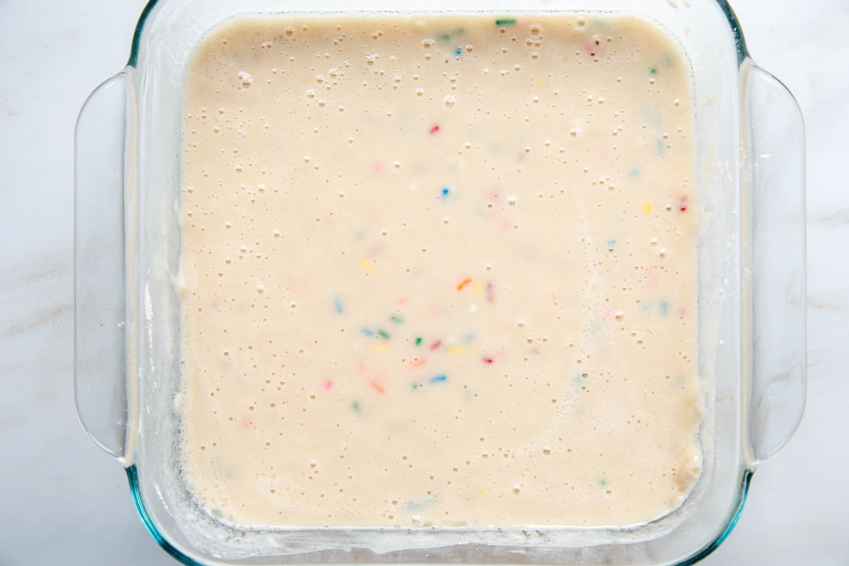 vanilla cake batter with sprinkles in a glass square dish.