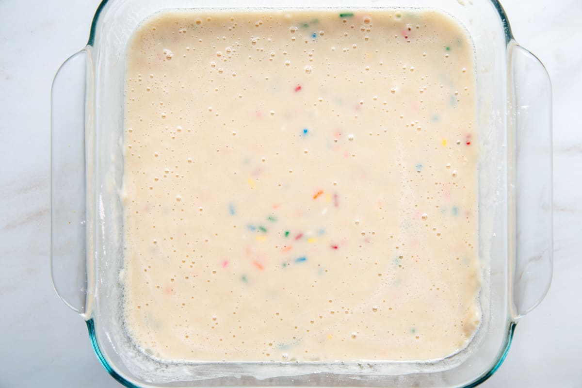 vanilla cake batter with sprinkles in a glass square dish.