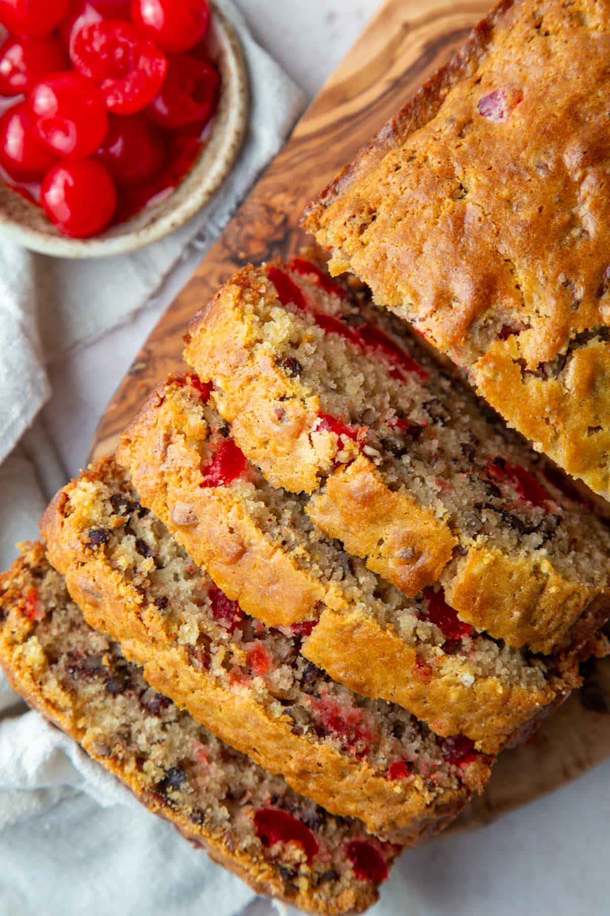 loaf of cherry bread with slices taken out next to a bowl of maraschino cherries.