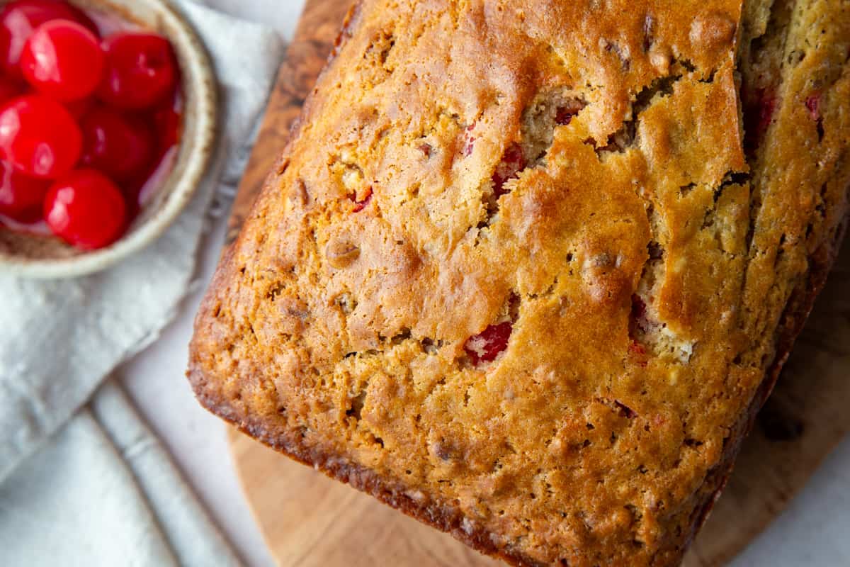 whole loaf of cherry bread next to a bowl of maraschino cherries.