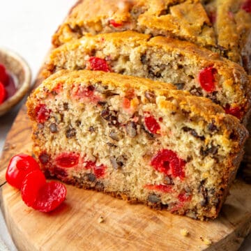 slices of cherry bread with pecans and maraschino cherries on a wooden board.