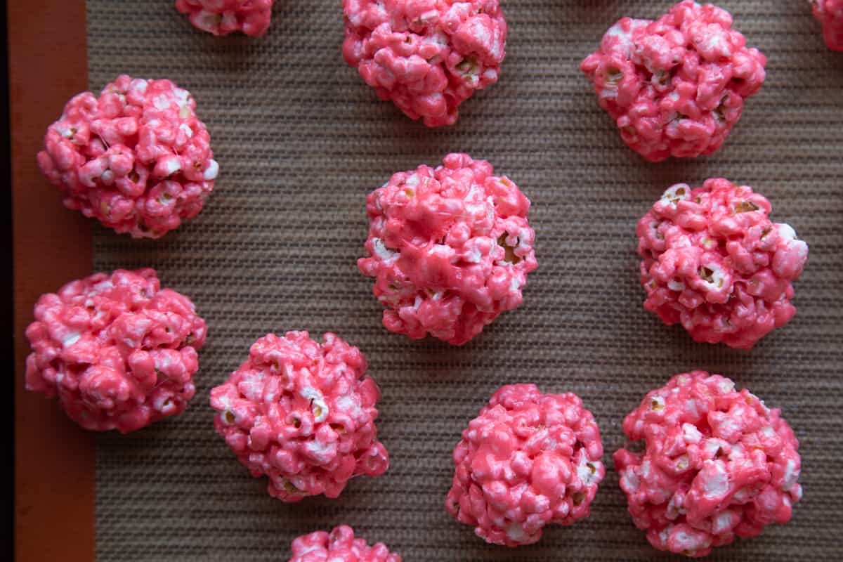 red marshmallow popcorn balls on a silicone mat. 