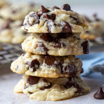 stack of four chocolate chip cookies with more cookies on a cooling rack in the background.