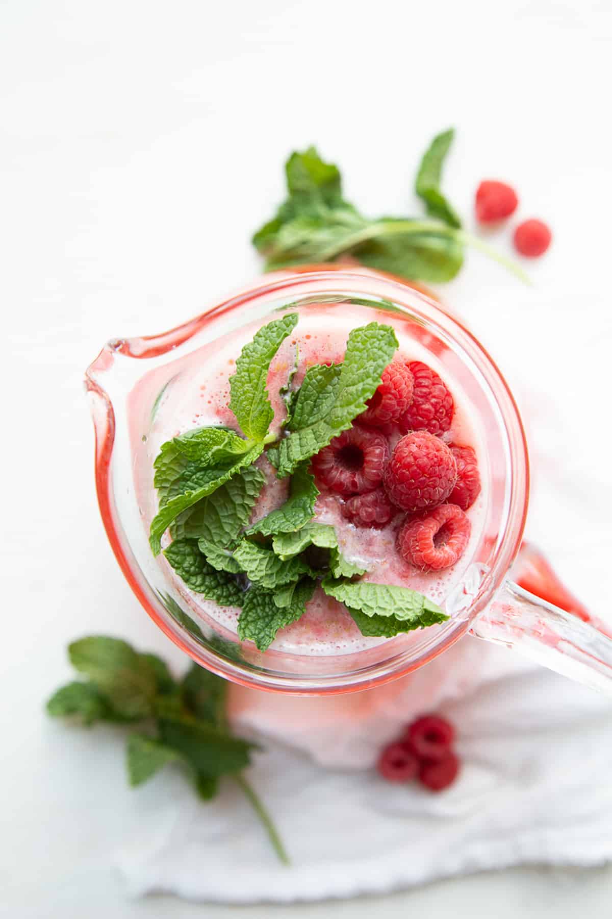 top-down view of a pitcher of raspberry lemonade garnished with fresh raspberries and mint leaves.