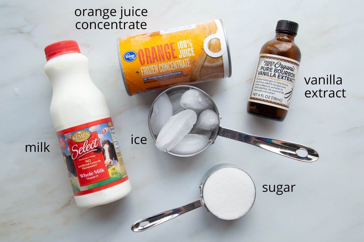 orange juice concentrate, sugar, milk, vanilla, and ice on a white table.